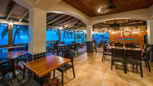 An indoor dining area with wooden tables and chairs, a view of the beach through large windows, and a sign that says "I ♥ BELIZE". - Sunbreeze Hotel (San Pedro)