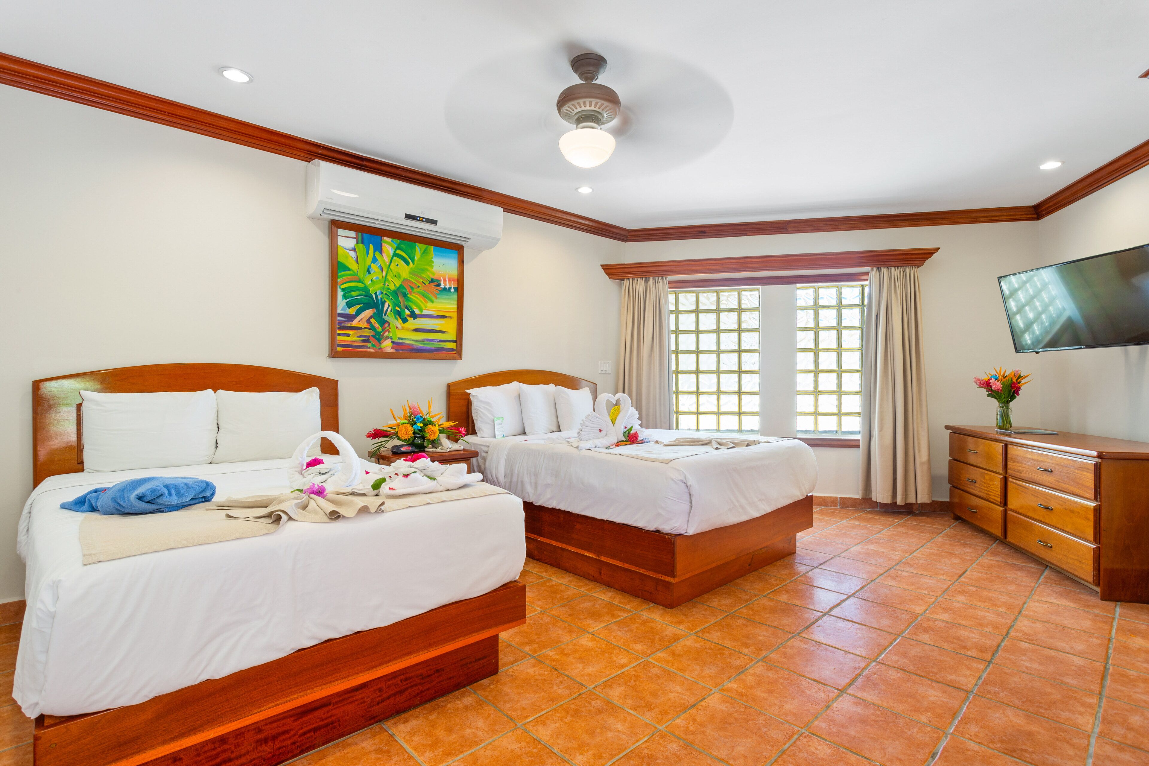 A hotel room with two beds, a TV, a painting, and a window with curtains.