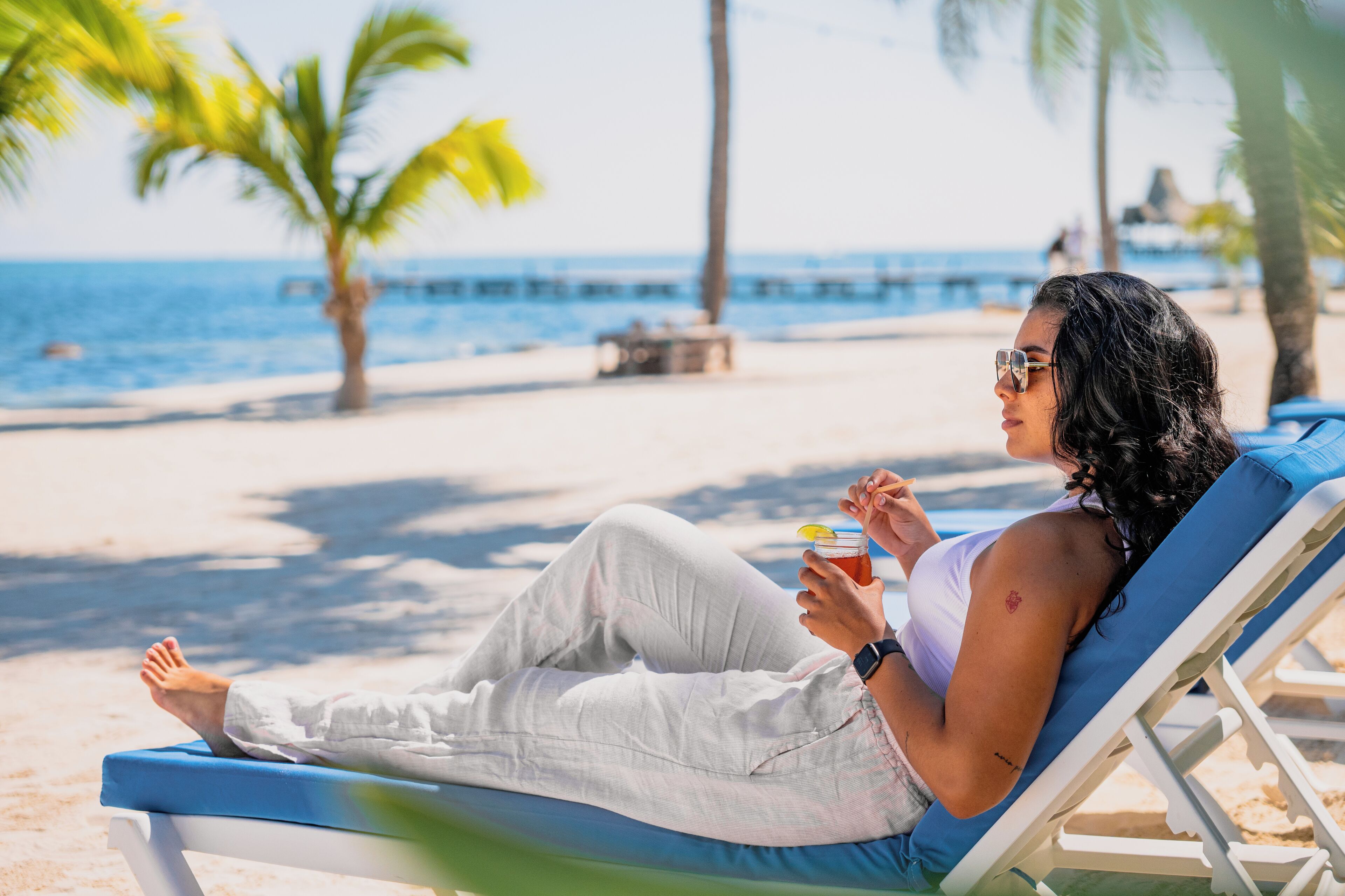 Eine Person entspannt sich in einem Liegestuhl am Strand mit einem Getränk und blickt aufs Meer.