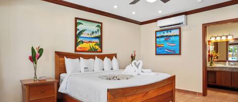 A wooden bed with white bedding, a nightstand with a vase of flowers, and two paintings on the wall depicting tropical scenes.