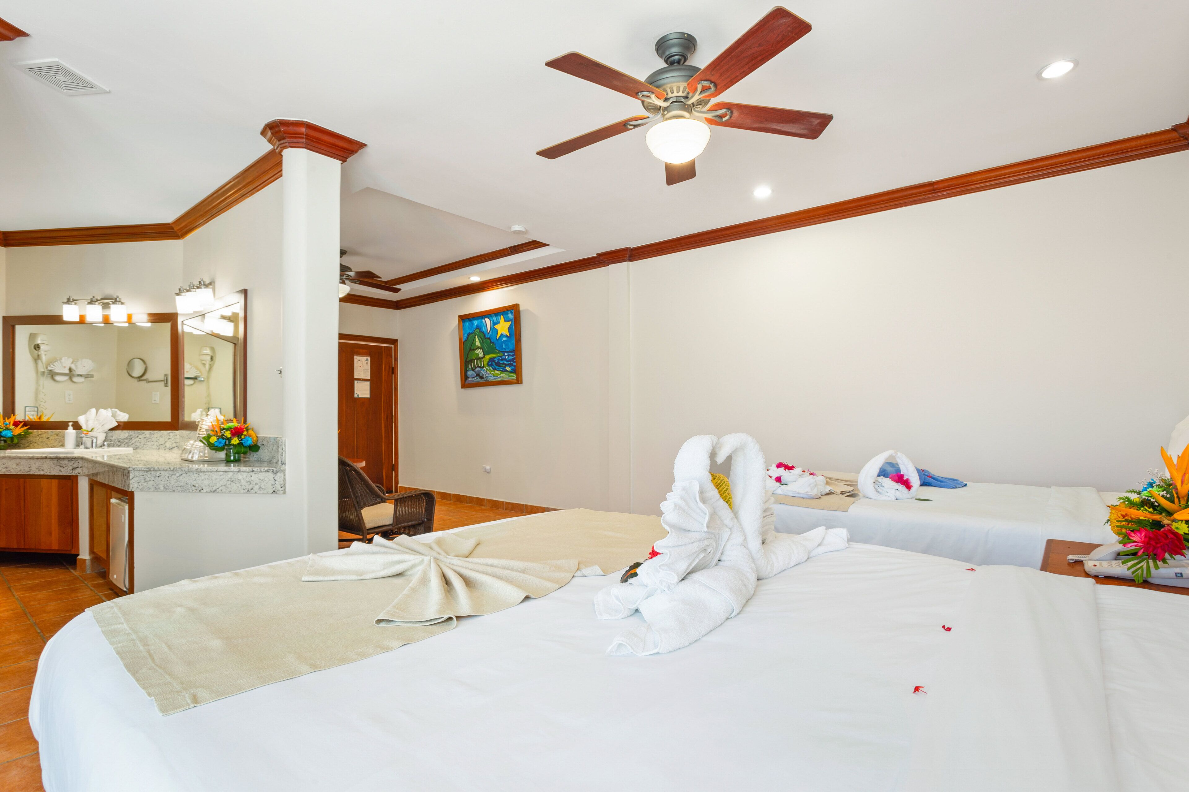 A hotel room with a bed, a desk, a chair, a bathroom, and a ceiling fan.