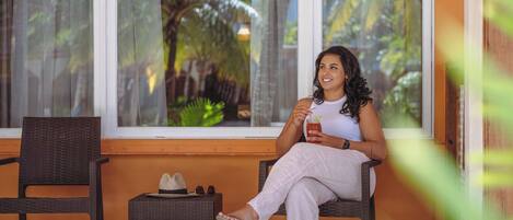 A person sitting on a wicker chair by a window with a view of palm trees.