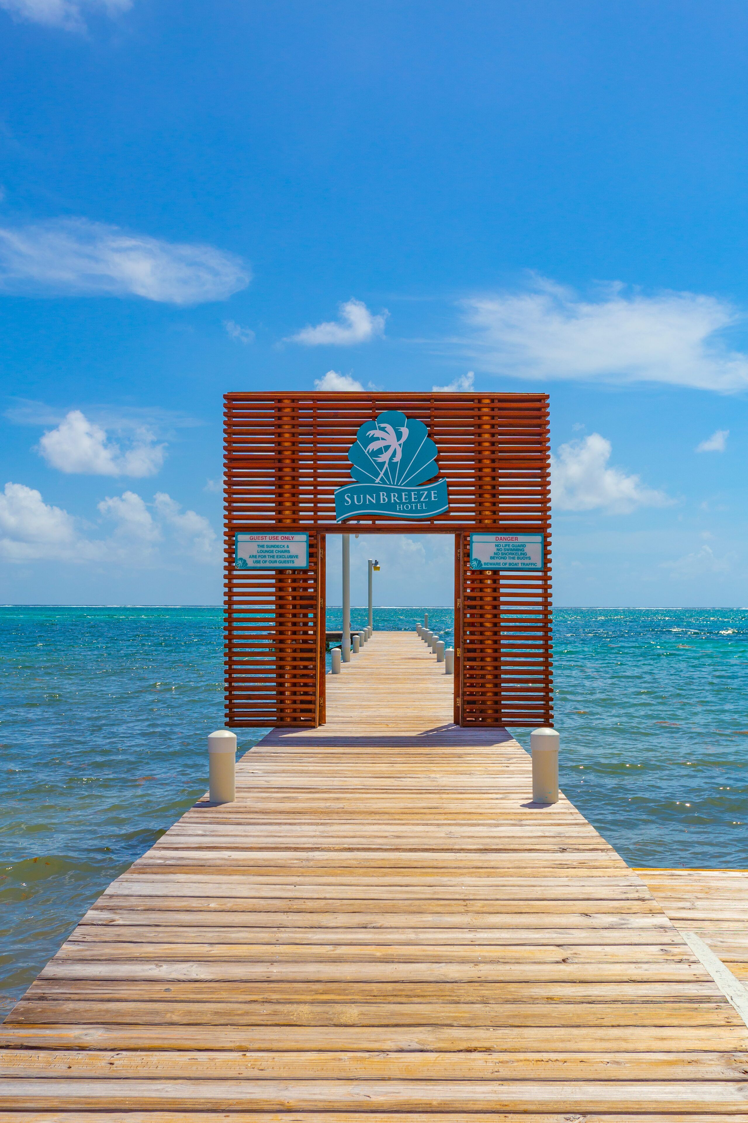 Un muelle de madera que lleva a la entrada de un hotel, con vista despejada al océano.