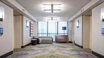 A hotel hallway with a patterned carpet, a sofa, a bench, and a large window with curtains.