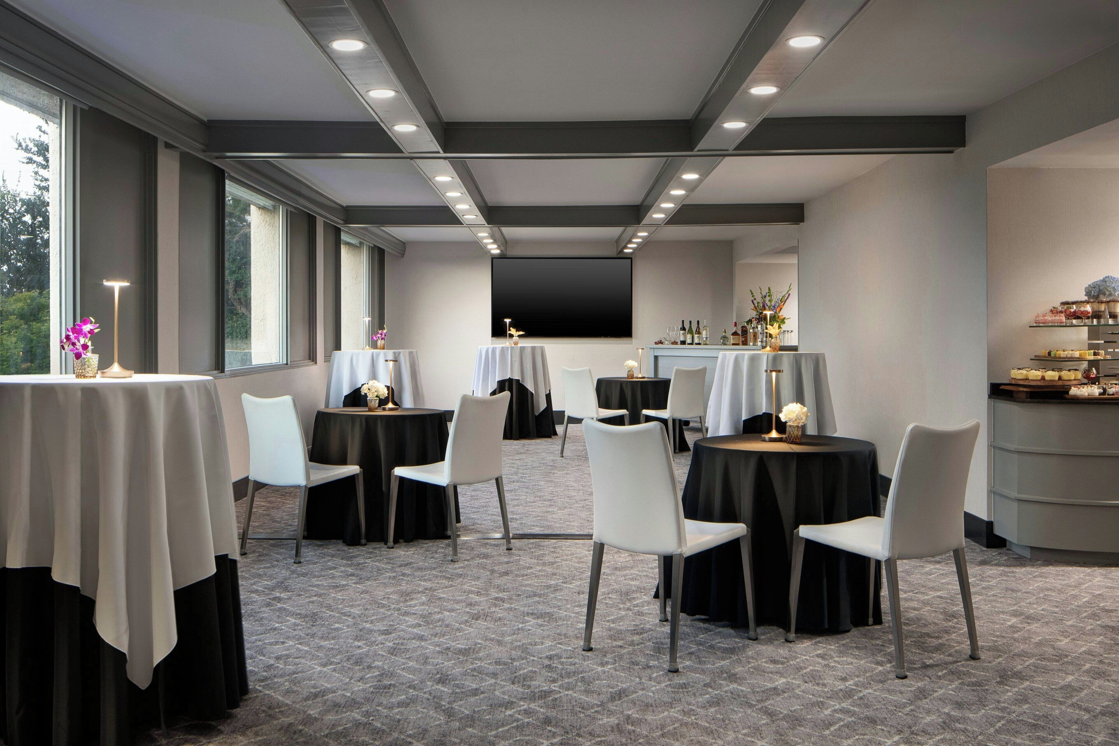 A modern conference room with round tables, white chairs, and a large screen.