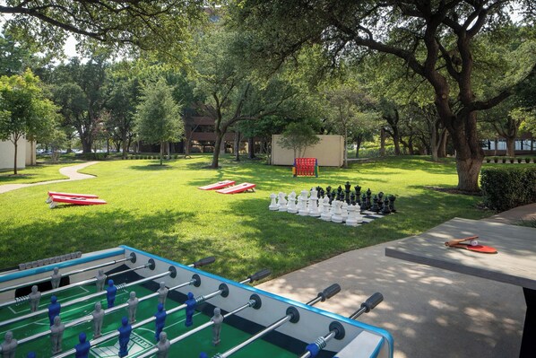 A park with a foosball table, a chessboard, and a table tennis table.