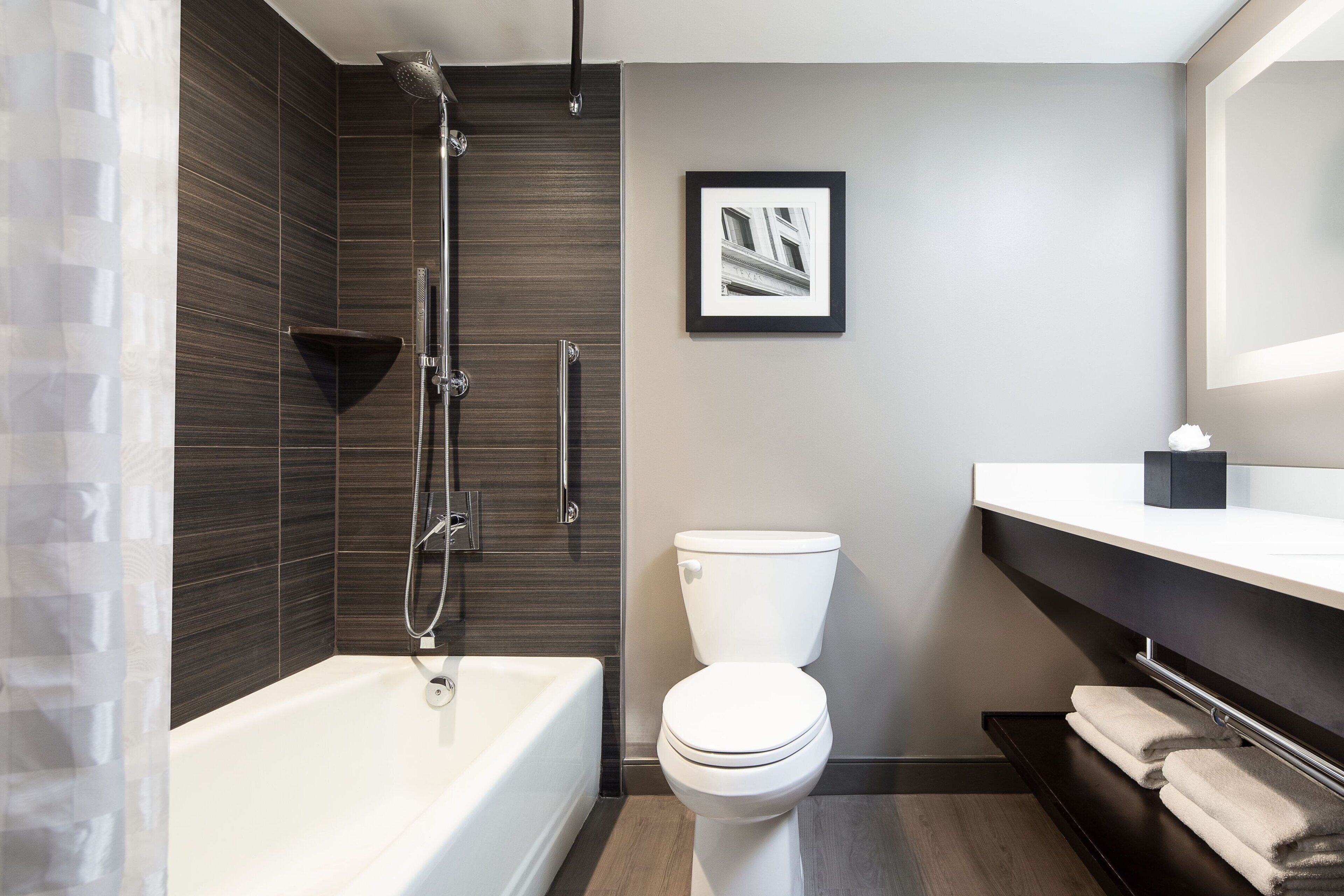 Ein modernes Badezimmer mit einer Badewanne, einer Toilette und einer Dusche. An der Wand hängt ein gerahmtes Bild und es gibt einen Handtuchhalter.