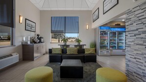 A modern lobby with a sofa, ottomans, a refrigerator, and a large window. - Hotel 28 Boise Airport, an Ascend Collection Hotel (Boise)