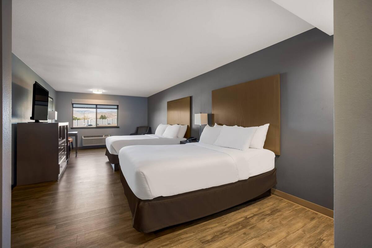 A hotel room with two beds, a desk, and a large window with a view.