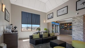 A modern living room with a sectional sofa, a coffee station, a large window with a view, and a kitchen area in the background. - Hotel 28 Boise Airport, an Ascend Collection Hotel (Boise)