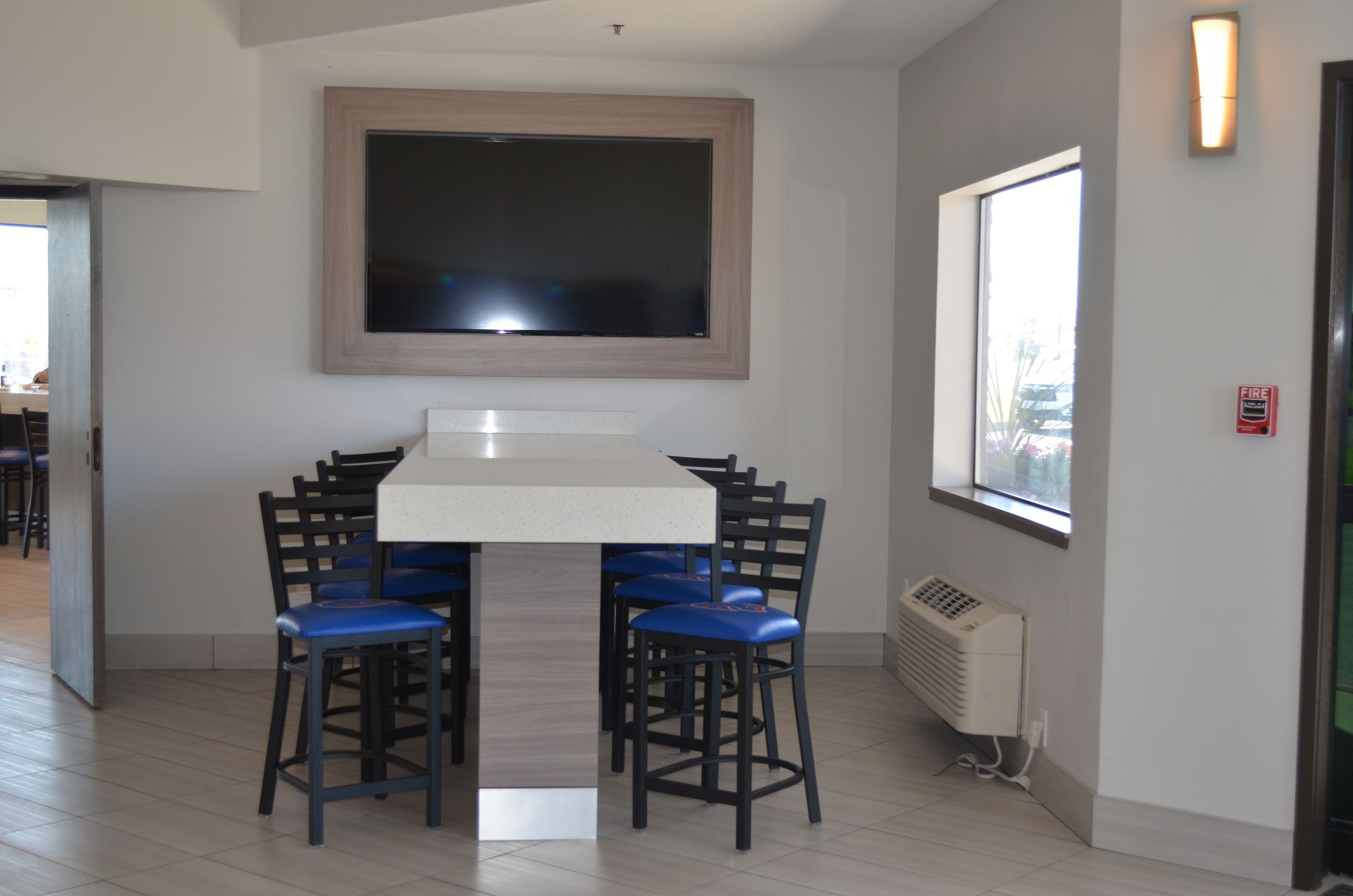 A modern dining area with a large flat-screen TV mounted above a white table surrounded by four blue chairs.