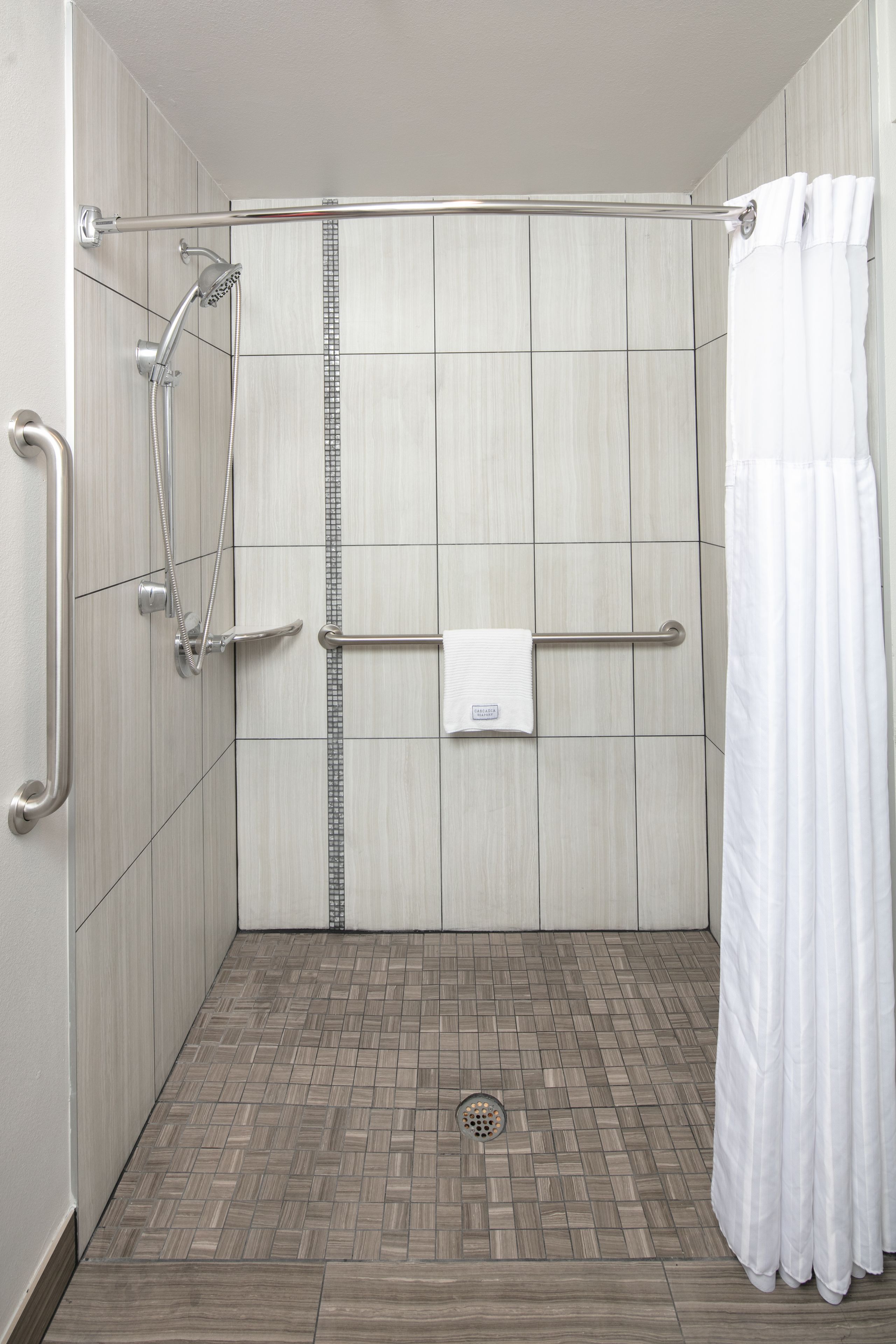 A shower area with a tiled floor, a showerhead, a towel rack, and a white shower curtain.