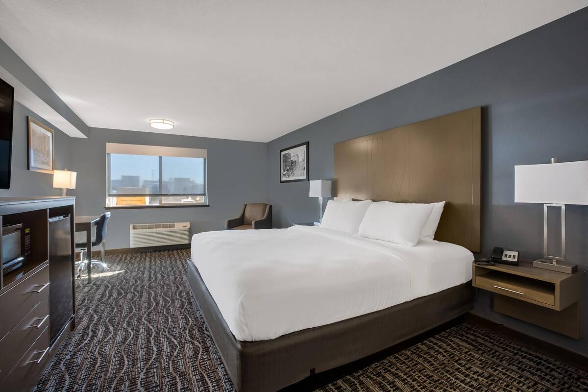 A hotel room with a large bed, a desk, a chair, a TV, and a window with a city view.