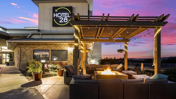 A hotel exterior with a sign reading "HOTEL 28," outdoor seating with a fire feature, and a stone facade. - Hotel 28 Boise Airport, an Ascend Collection Hotel (Boise)
