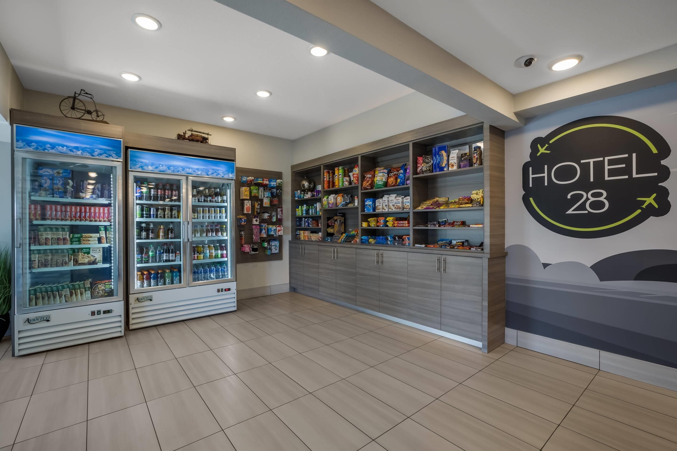 Um saguão de hotel com dois dispensadores de bebidas, um bar de lanches e um letreiro 'HOTEL 28'.