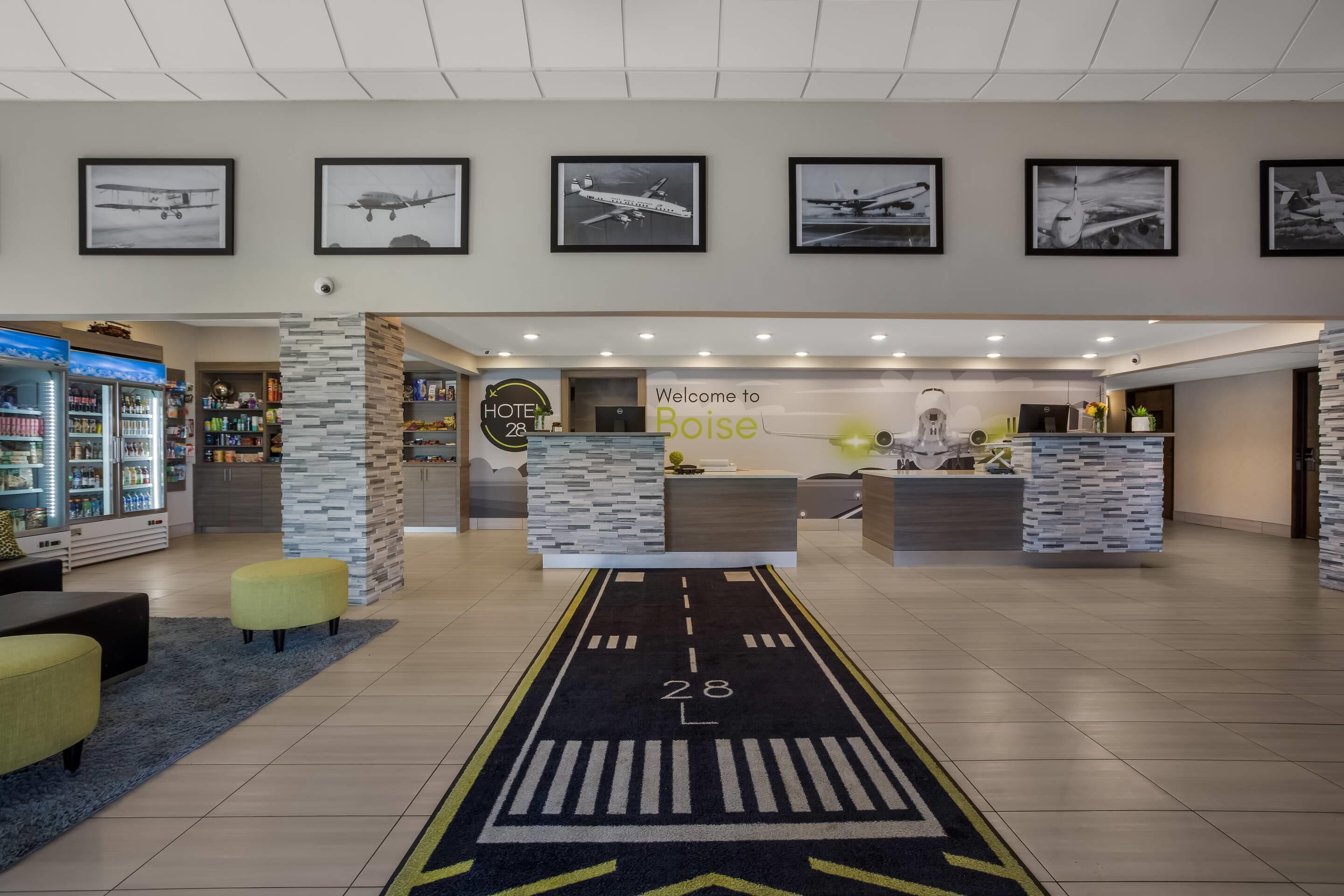 A hotel lobby with a reception desk, framed airplane pictures on the wall, a welcome sign, and a carpet with a runway design.