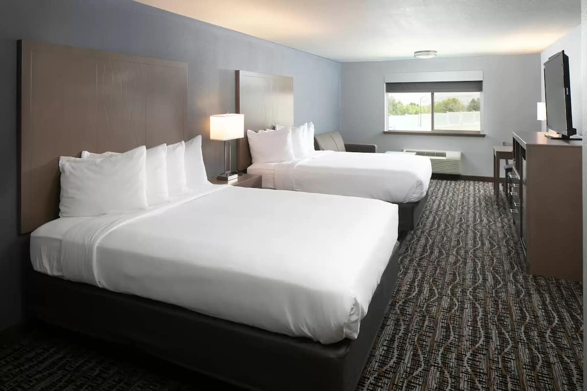 A hotel room with two beds, a desk, a television, and a window.