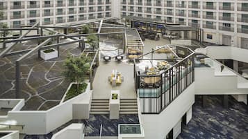 A modern hotel atrium with multiple levels, outdoor seating areas, and a central staircase.