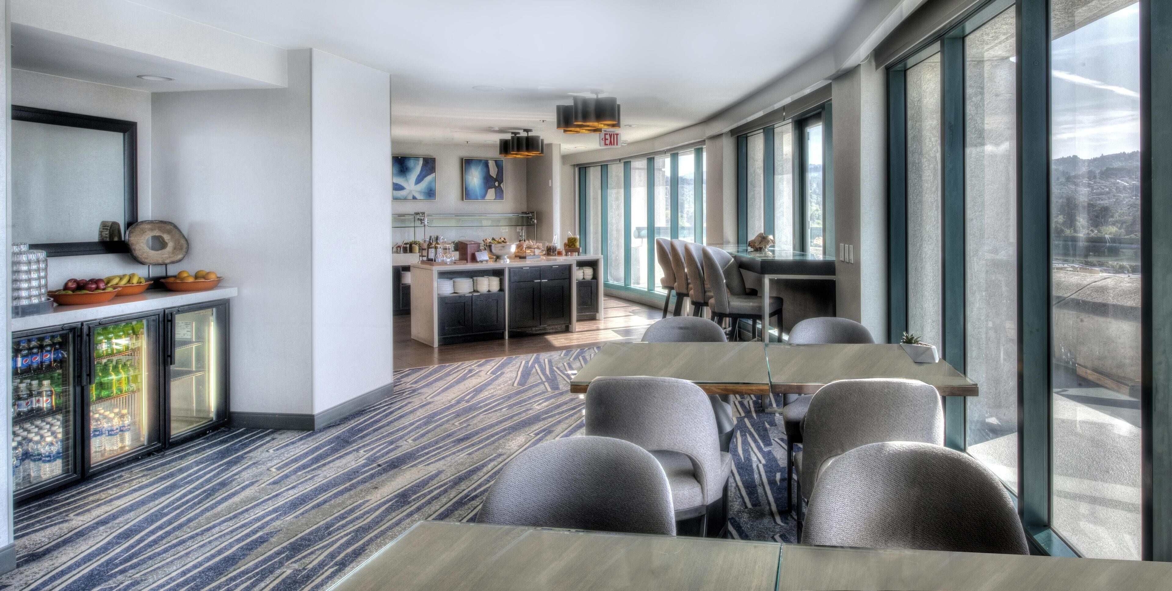 Una habitación de hotel moderna con comedor, ventanas amplias y vistas al exterior.