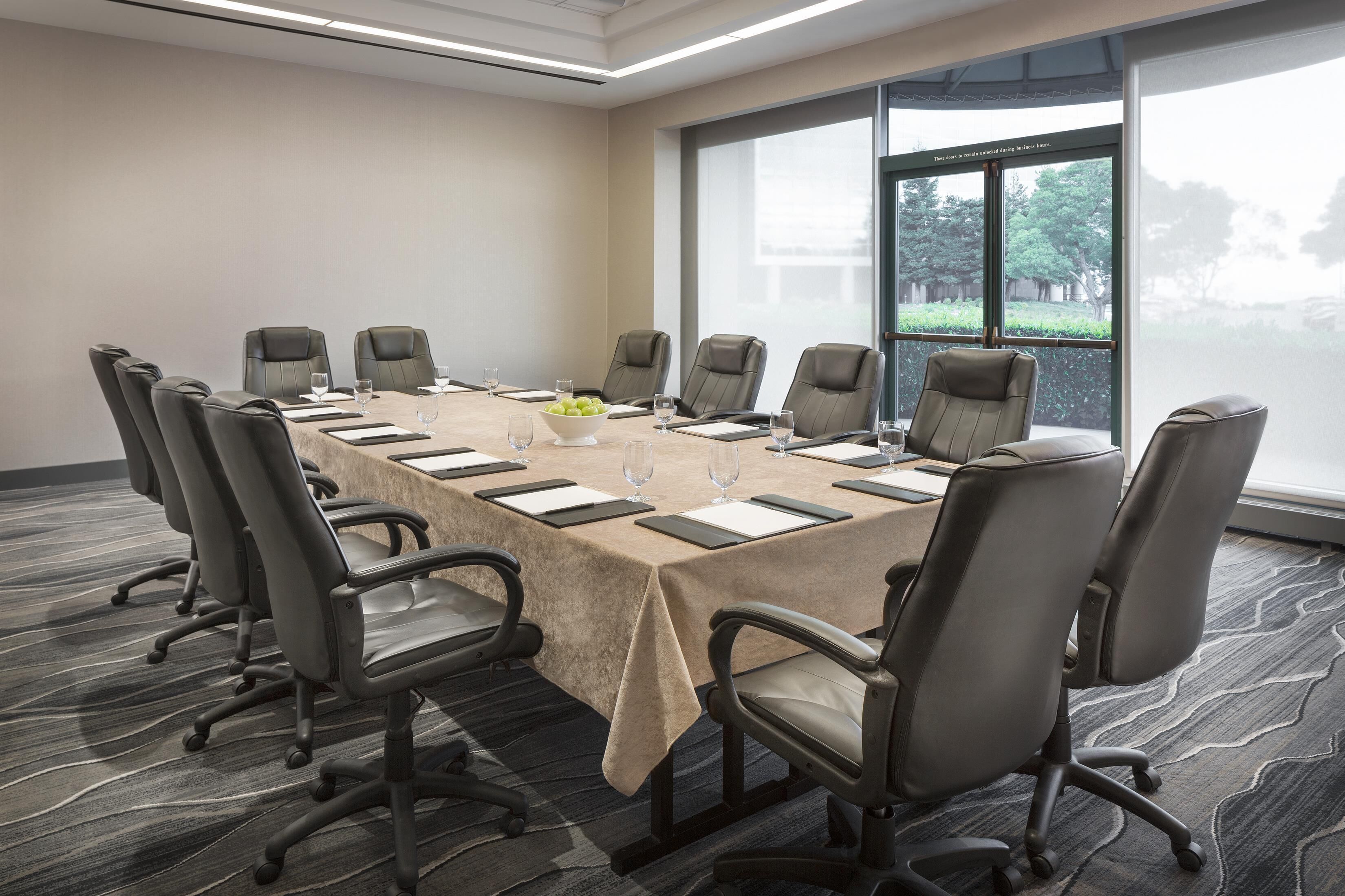 Une salle de conférence avec une longue table, des chaises et une fenêtre donnant sur des arbres.