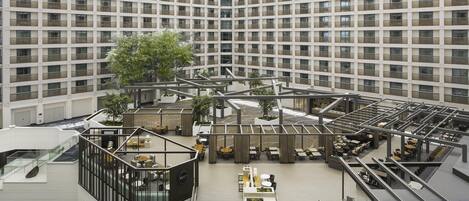 A modern hotel atrium with a central open space, multiple floors, and a glass ceiling.