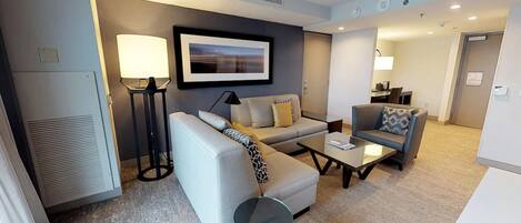 A modern living room with a sofa, armchair, and coffee table. There is a framed picture on the wall, a floor lamp, and a radiator.