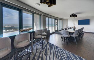 Un salón de conferencias moderno con amplios ventanales, una vista panorámica del mar y una lámpara de araña contemporánea.
