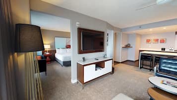 Quarto de hotel com cama, escrivaninha, televisão, minibar e área de estar.