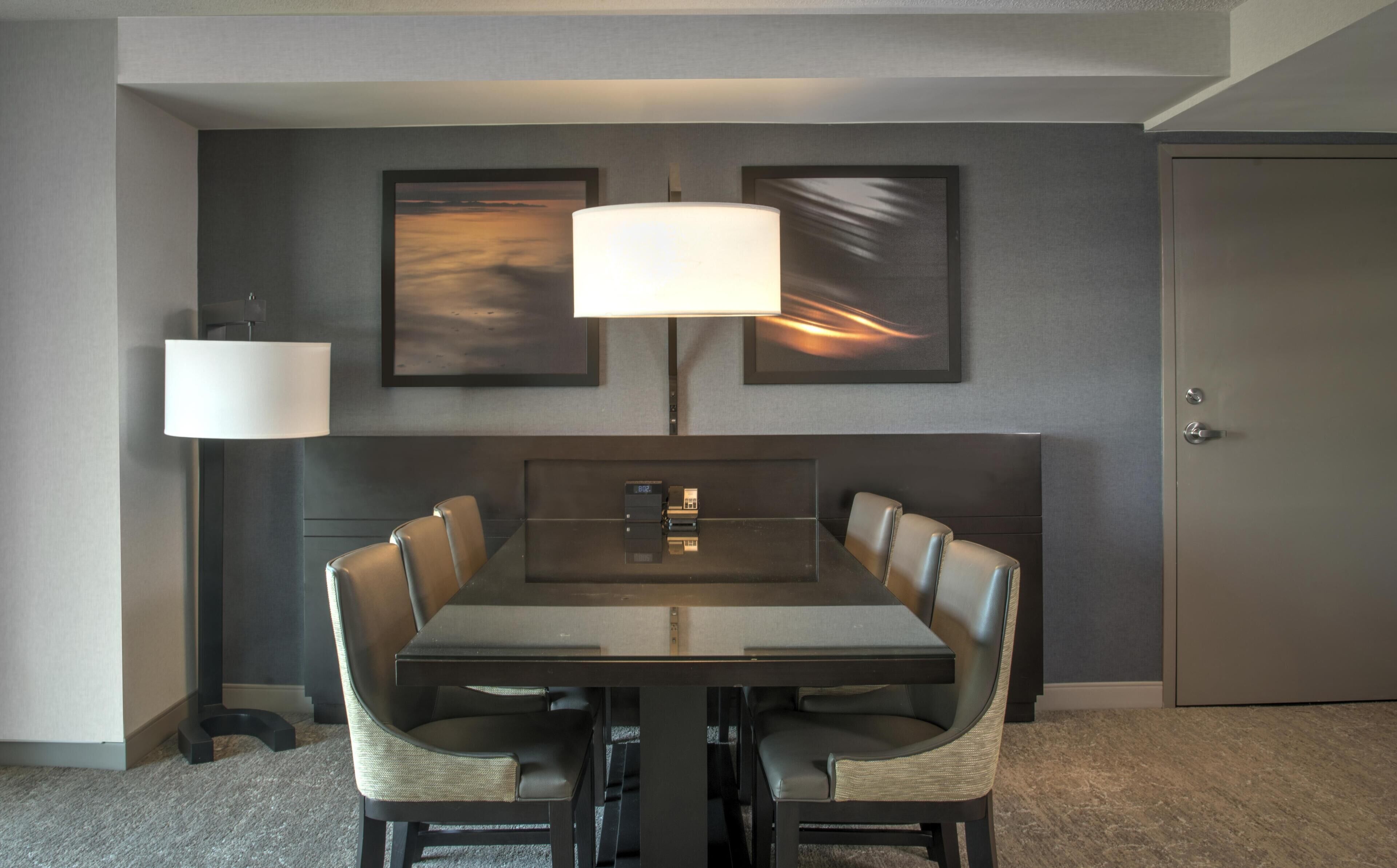 Una habitación de hotel con una mesa de comedor, sillas, una lámpara y obras de arte en la pared.