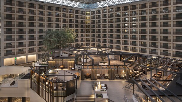 Un vestíbulo de hotel de varios niveles con un espacio central abierto, múltiples zonas de estar y un techo de cristal.