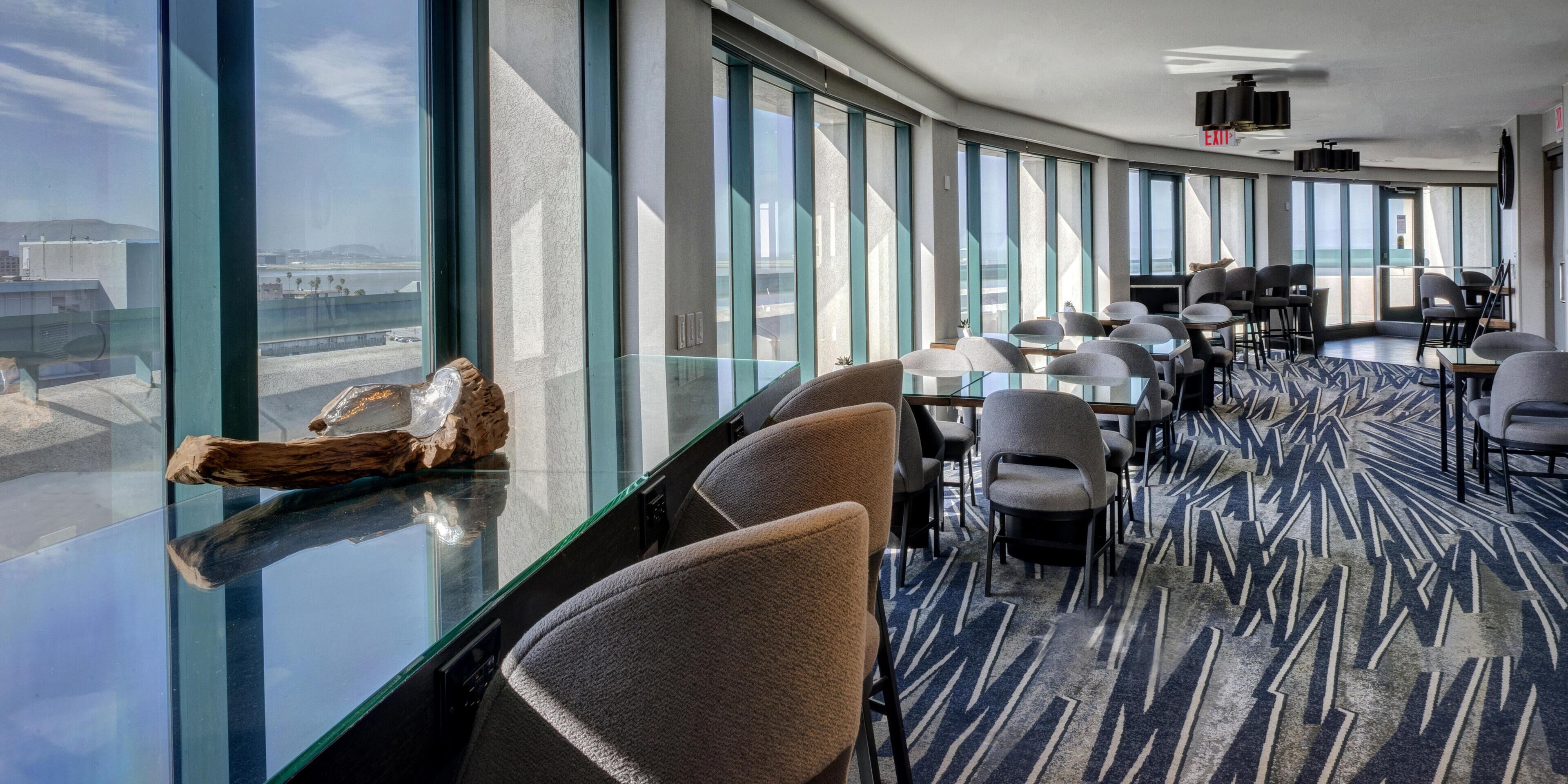 A modern hotel conference room with large windows, a glass table, and comfortable seating.