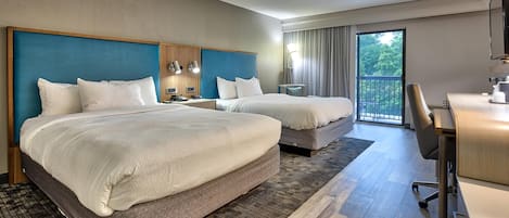 Habitación de hotel con dos camas, un escritorio, una silla, un televisor y un balcón con vistas.