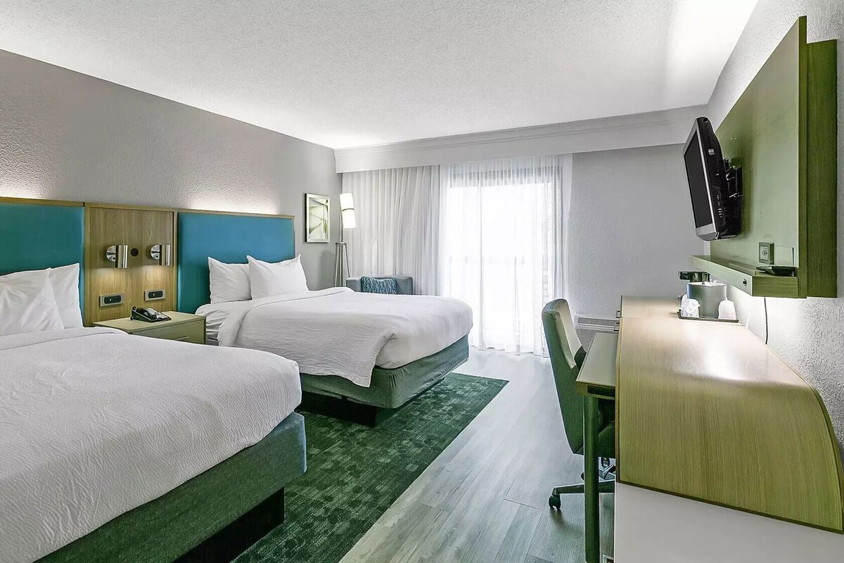 A hotel room with two beds, a desk, a chair, a TV, and a window with curtains.
