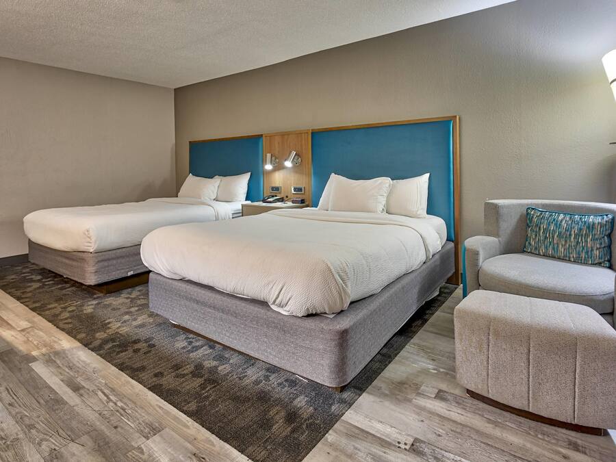 A hotel room with two beds, a sofa, a chair, and a lamp.
