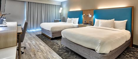 A hotel room with two beds, a desk, a chair, a desk lamp, a telephone, and a window with curtains.