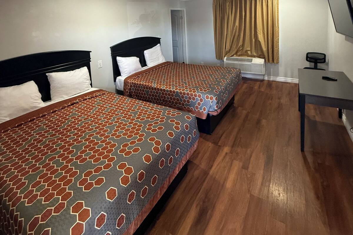 A hotel room with two beds, a desk, a TV, and a window with curtains.