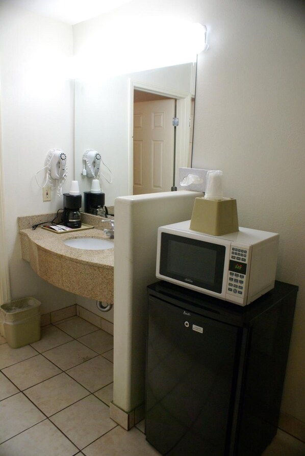 A compact hotel bathroom with a sink, a mirror, a microwave, and a small refrigerator.