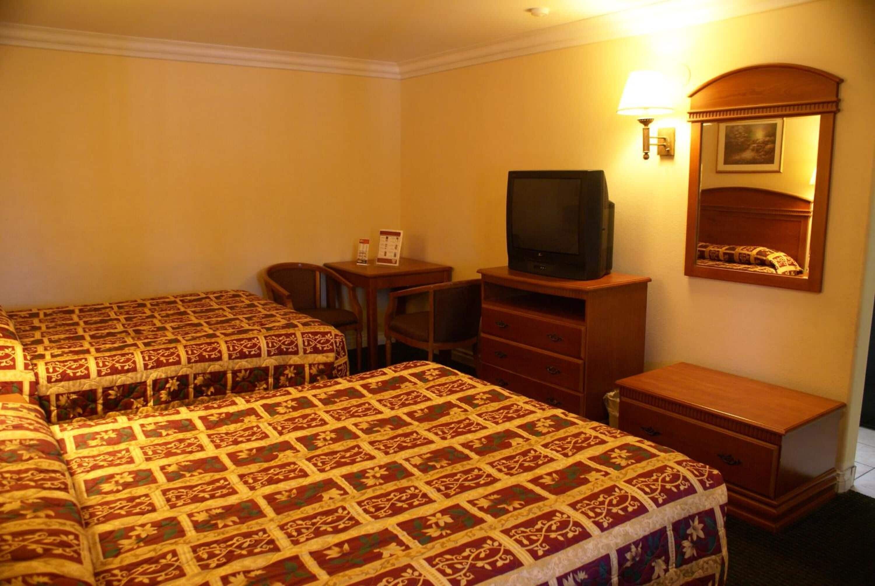 A hotel room with two beds, a desk, a chair, a television, a dresser, and a mirror.