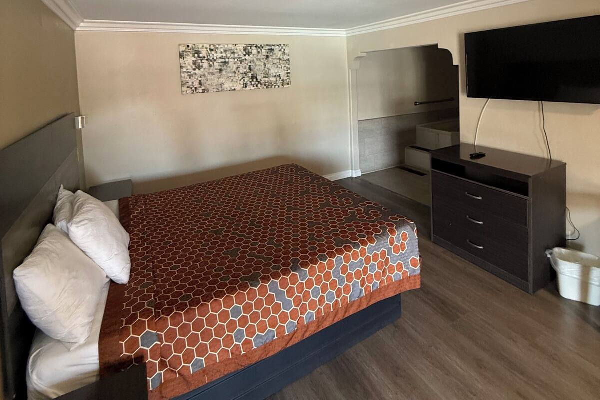 A bedroom with a bed, a dresser, a television, and a wall art piece.