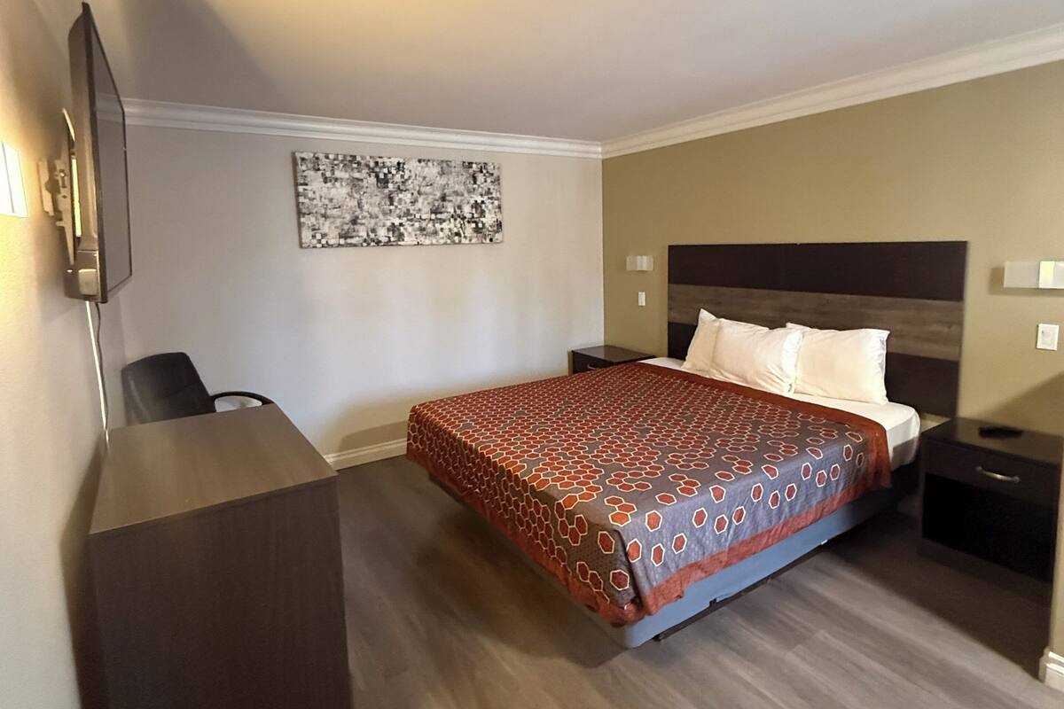 A hotel room with a bed, a desk, a chair, a TV, and a wall-mounted artwork.