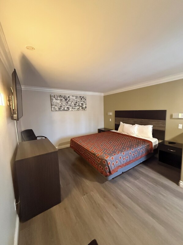 Una camera d'albergo con un letto, una scrivania, una sedia, una TV e un'opera d'arte appesa al muro.