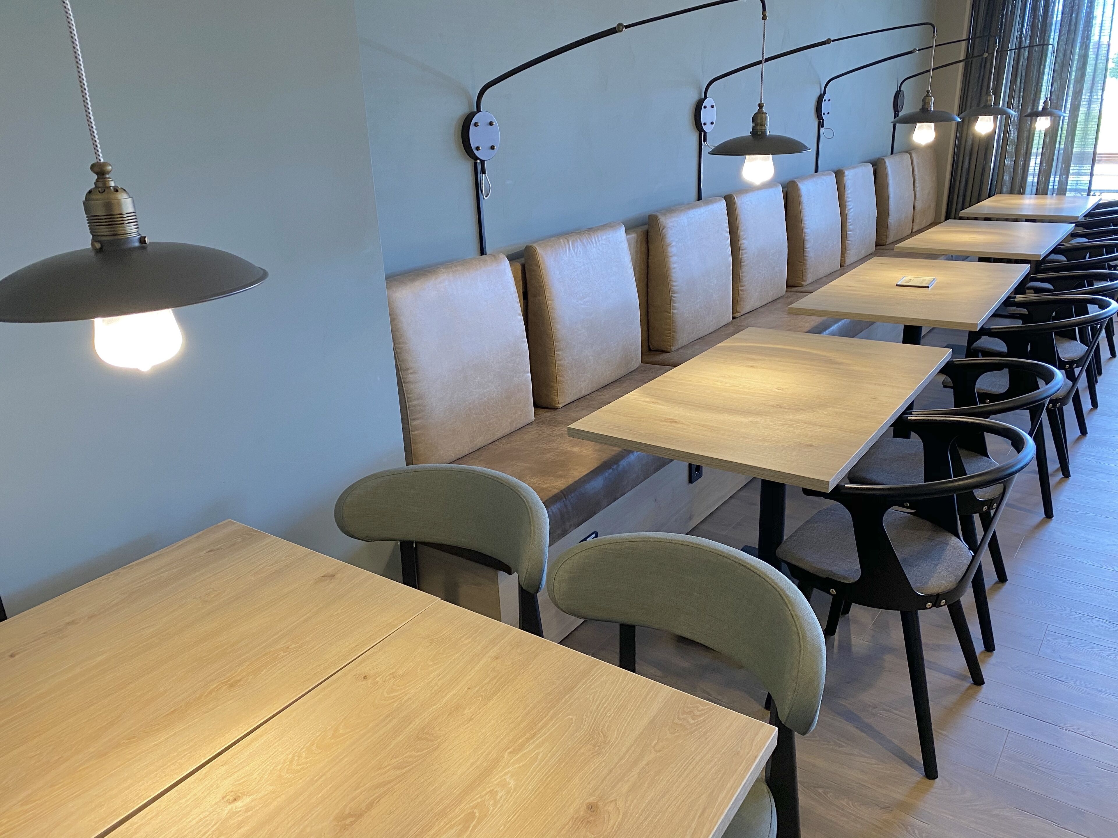 A restaurant with long wooden tables and cushioned booths, modern pendant lighting, and a clean, minimalist design.