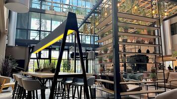 Un espace intérieur vaste et lumineux, doté d’un design moderne, comprenant une table centrale entourée de chaises, un escalier et une étagère agrémentée de plantes.