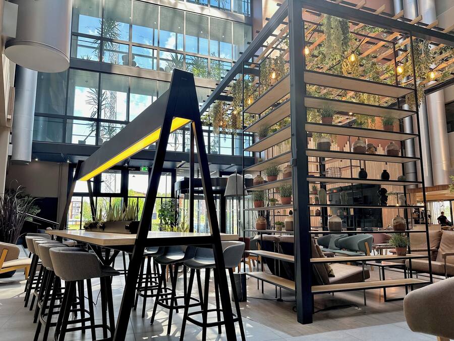 Un espace intérieur vaste et lumineux, doté d’un design moderne, comprenant une table centrale entourée de chaises, un escalier et une étagère agrémentée de plantes.