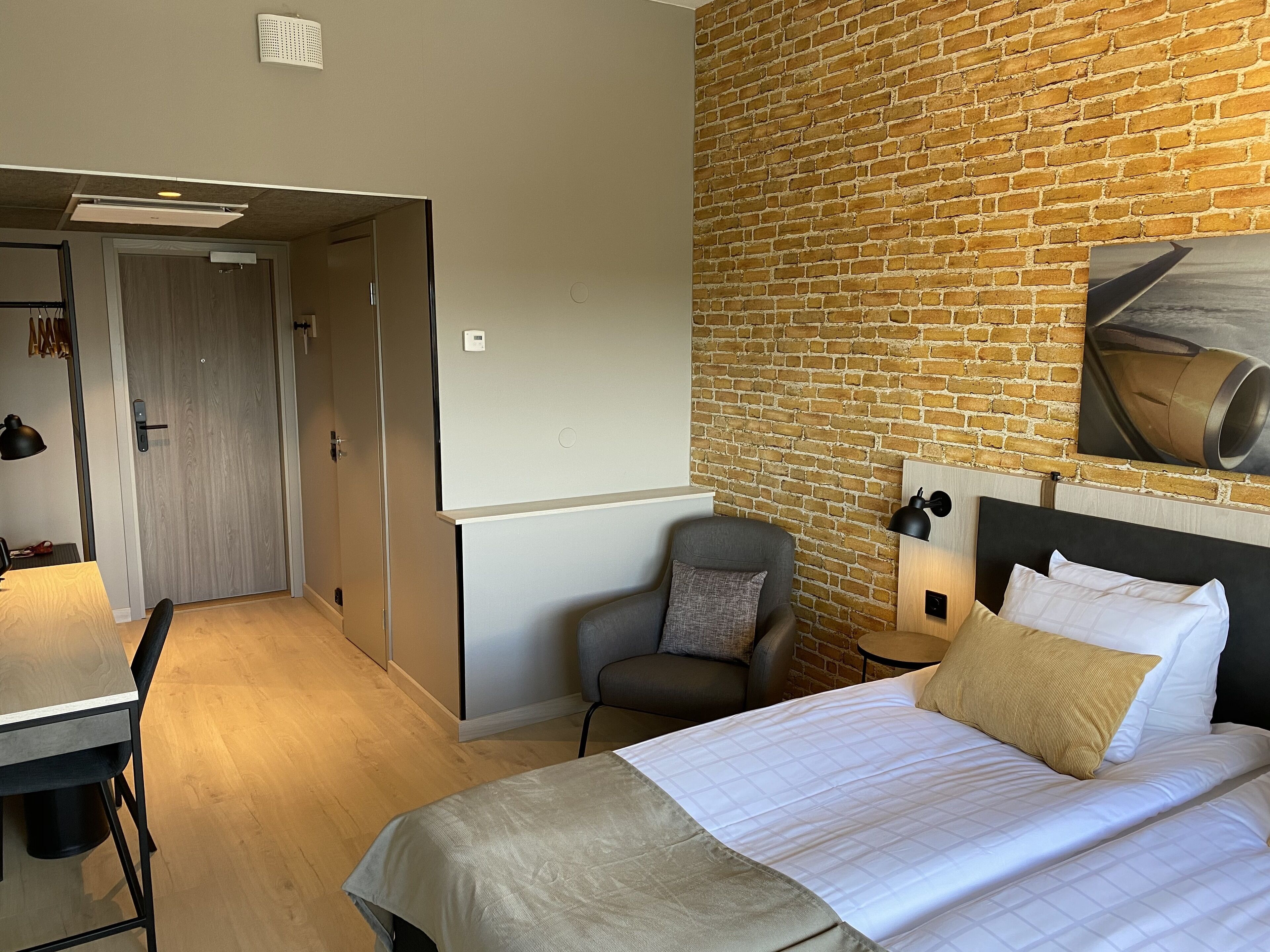 Hotellihuone, jossa on sänky, työpöytä, tuoli ja tiiliseinä.