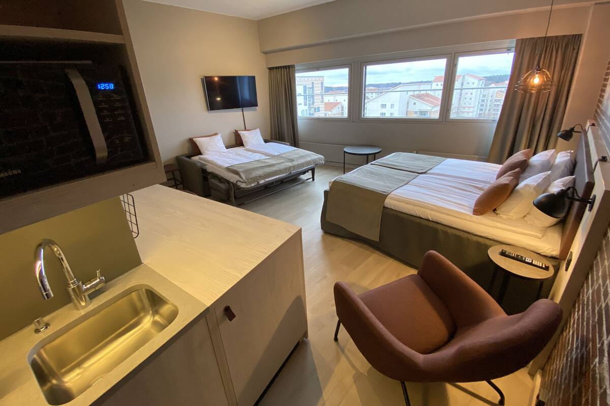 A hotel room with a bed, a sofa bed, a small table, a TV, a sink, and a chair.