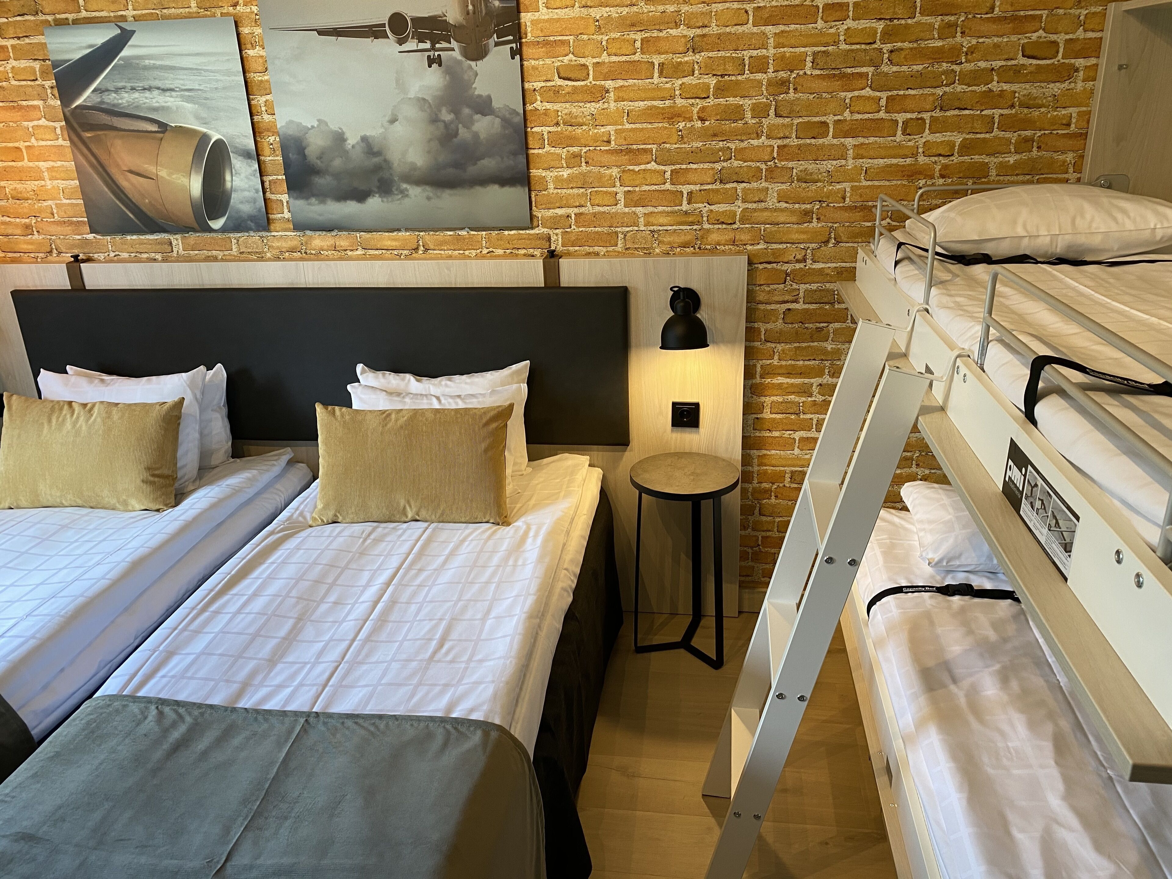 A hotel room with two beds, a small table, and a bunk bed.