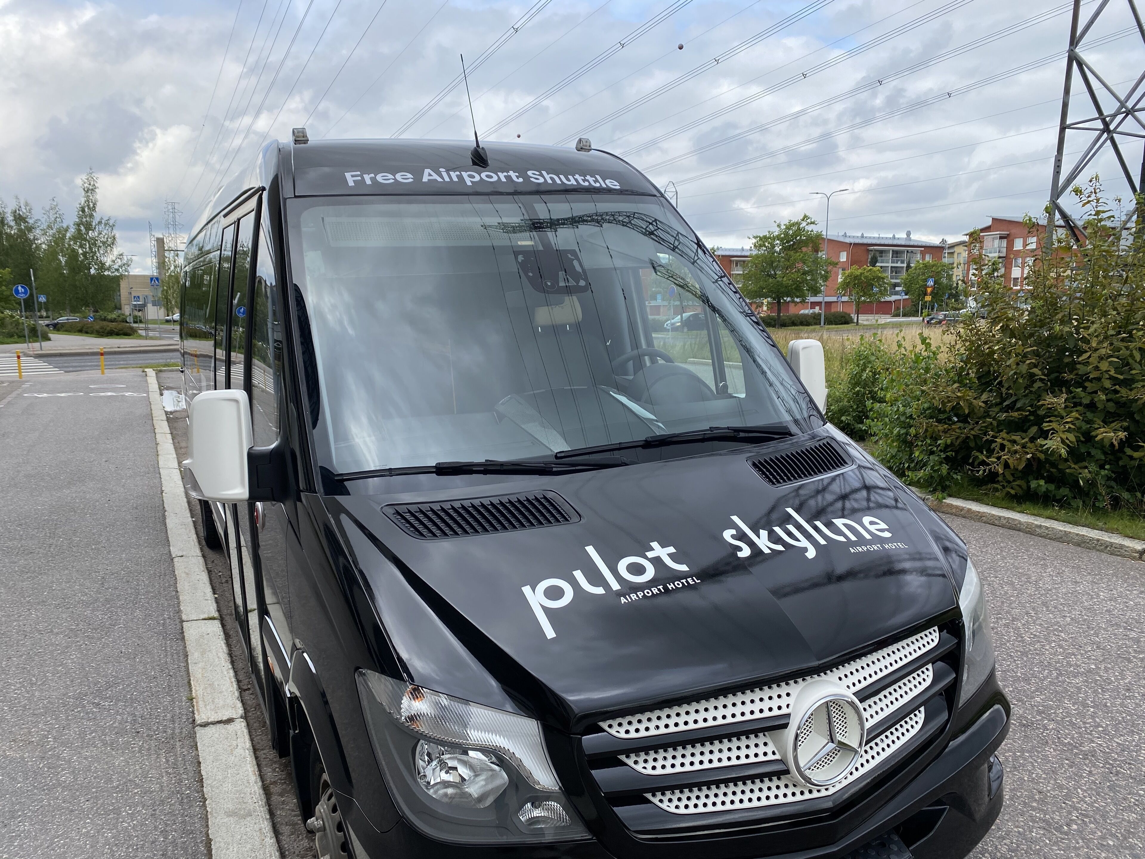 Musta lentokenttäbussi, jonka etuosassa on teksti: ”Ilmainen lentokenttäkuljetus” ja ”Pilot Skyline -hotelli”.