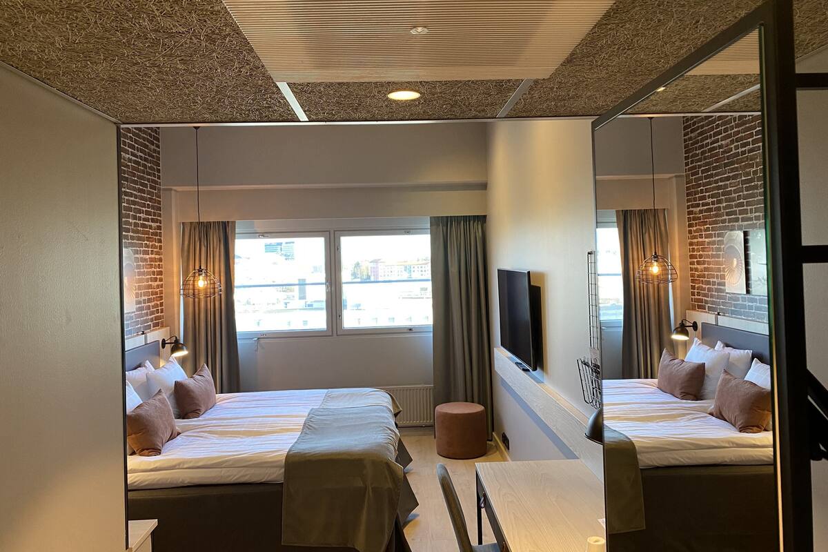 A hotel room with two beds, a TV, a mirror, and a window with curtains.