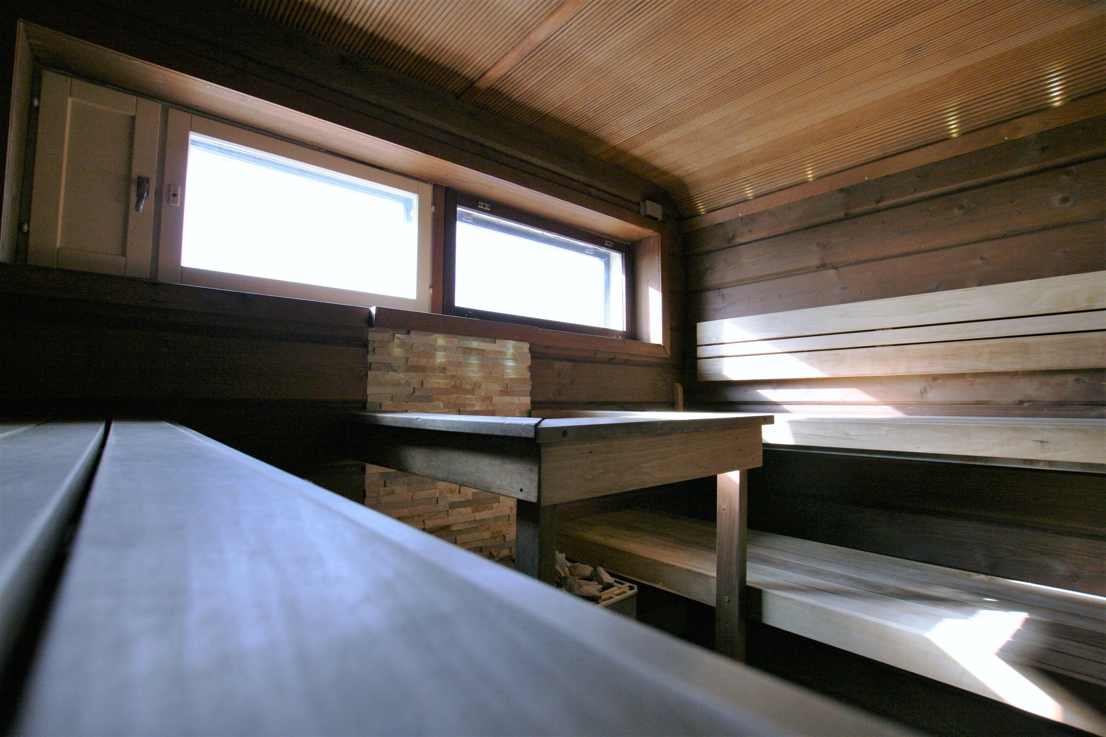 Interior de una cabaña con un banco de madera, una mesa y un ventanal con vistas.